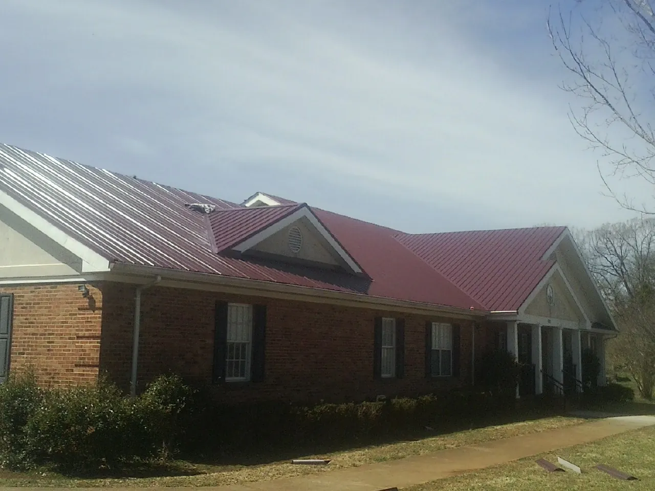 Red metal roof with gabled entries on a long brick building, from a Hail Damage Roof Repair job in Sedona