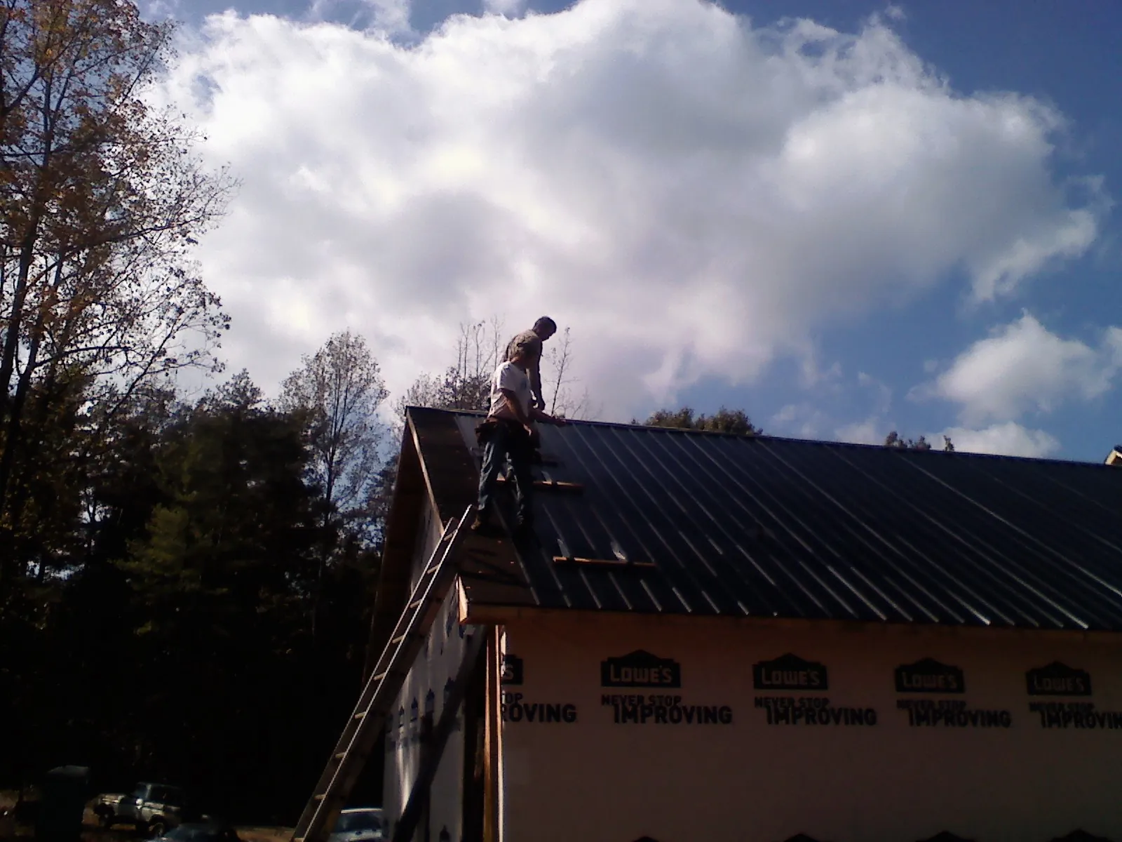 Roofer fastening dark metal panels high against a cloudy sky, from a Roof Inspection job in Sedona